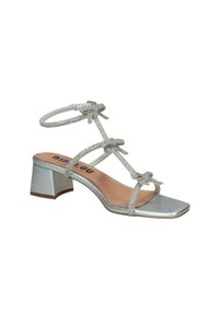 Sandal con tacco quadrato in argento, con cinturini alla caviglia e fiocchi decorativi. La parte superiore presenta un materiale scintillante, completato da un tacco a blocco metallico.
