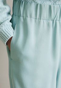 Vaaleansiniset kangasfarkut, joissa on teksturoitu vyötärö, sivutaskut ja kapeneva lahjemuoto. Pehmeä ja sileä pinta kauttaaltaan.