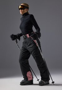 Ski outfit featuring a fitted black top and insulated black pants with pink accents. Ski poles in hand, wearing large ski goggles.