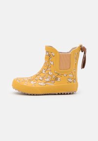 Bota tobillo de caucho amarilla con patrón floral, suela texturizada, paneles laterales elásticos y lazo en el talón para facilitar su uso. Acabado liso y detalles con costuras.