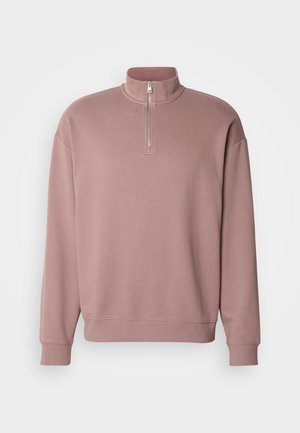 Vaaleanpunainen vetoketjullinen huppari korkealla kauluksella ja ribbineuloksella. Edessä on huomaamaton logotaito. Pehmeä materiaali.