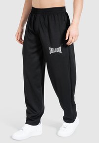 Schwarze Sporthosen mit strukturiertem Finish und einem elastischen Bund, mit weißem "SMILODOX"-Logo auf der Vorderseite. Kombiniert mit weißen sneakers.