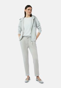 Hellgraue Zip-Hoodie mit Fronttaschen, kombiniert mit passenden Jogginghosen mit Kordelzug und silbernen Ballerinas.