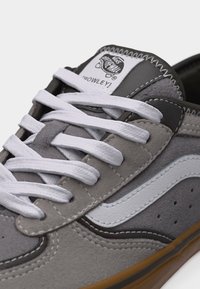 Γκρι και μαύρο παπούτσι Vans με λευκή λωρίδα στο πλάι και κορδόνια, με λεπτομέρειες από σουέτ και ραφές, και σόλα από καουτσούκ σε χρώμα καραμέλας.