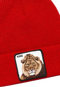 Beanie rosso lavorato a maglia con un'etichetta quadrata che presenta un leone ricamato e la parola "KING" sopra di esso. Materiale testurizzato e design aderente.