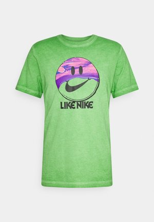 Vihreä puuvillatee paita, jossa on pyöreä hymyilevä kasvokuva violetilla korostuksella ja teksti "LIKE NIKE" paksulla mustalla fontilla.