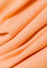Pfirsichfarbener Strickstoff, glatte Textur mit einem leichten, leicht dehnbaren Design. Sichtbare gerippte Kanten und unterschiedliche Stofffalten.