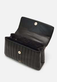 Sac à main en cuir matelassé noir avec une fermeture à pression dorée et deux compartiments principaux. L'intérieur présente une doublure à motifs et une poche zippée.