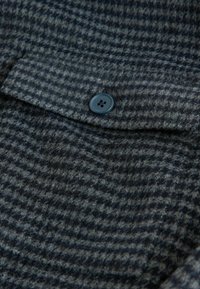 Gewebter Stoff in dunkelgrau mit einem karrierten Muster; hat einen sichtbaren Knopf auf der Tasche; weiche Textur und subtiler Glanz.