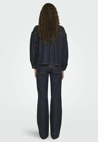 Tumman denim-takki leveillä hihoilla ja soveltuvilla leveälahkeisilla housuilla. Näkyvät ompelusaumadetailit ja takataskut. Sileä, teksturoitu kangas.
