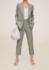 Costume vert clair ajusté avec blazer croisé et pantalons slim. Débardeur blanc, sac en tissu blanc tissé et sandales à lanières.