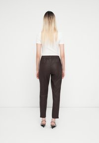 Pantalones marrones ajustados con una cintura elástica, con bolsillos traseros, combinados con una camisa blanca de manga corta y sandalias negras de tacón.