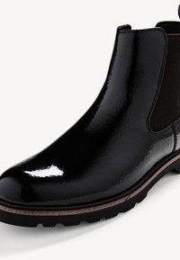 Botte Chelsea en cuir noir brillant avec panneau latéral élastique et semelle en caoutchouc robuste sur un fond clair uni.