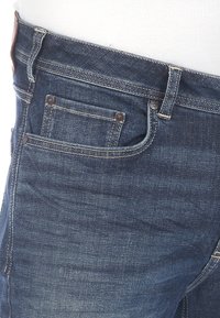 Jeans in denim blu scuro, caratterizzati da un classico design a cinque tasche, dettagli di cucitura e una texture liscia con una patch in pelle sulla vita.