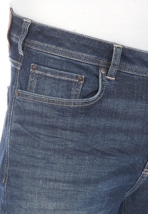 Dunkelblaue Denim-Jeans im klassischen Five-Pocket-Design, mit stolzierenden Nähten und einer glatten Textur sowie einem Lederpatch am Bund.
