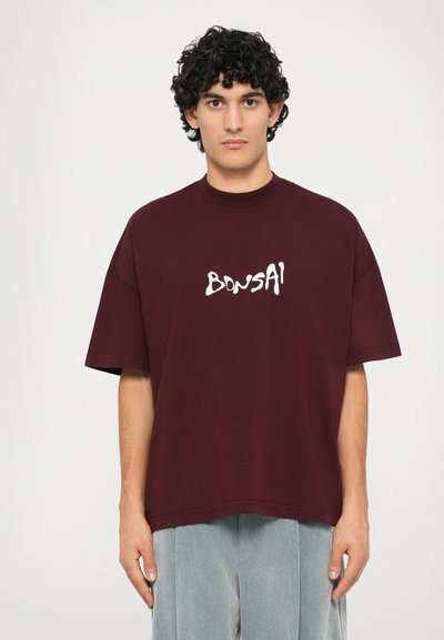 Burgundijas krāsas pārāk liels T-krekls no kokvilnas ar baltu "BONSAI" teksta logotipu, apaļu dekoltē un īsām piedurknēm. Gluda tekstūra.