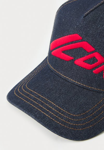 Tumesinine denimplaat, millel on punane tikandiga logo. Omab nähtavat õmblust ja kumerat sapka. Tekstureeritud kangast viimistlus.