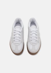 Baskets blanches avec une tige synthétique lisse, bout rond et semelle extérieure en gomme texturée. Caractéristiques : lacets plats et col rembourré.