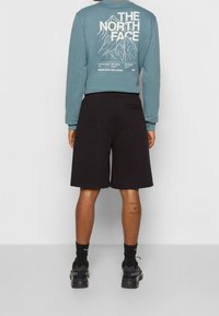 Světle modrý svetr s grafickým motivem hory a textem na zádech, doplněný černými šortkami. Ležérní střih, měkká tkanina a elastický pas.