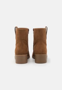 Braune Wildleder-Stiefeletten mit glatter Oberfläche, Reißverschluss und kurzen Blockabsätzen. Rückansicht, die das nahtlose Design hervorhebt.
