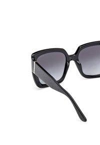 Gafas de sol negras con una gruesa montura rectangular y lentes degradados. Patillas texturizadas en negro con un acento metálico cerca de la bisagra.