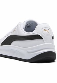 Fehér sneaker fekete részletekkel, sima bőr anyagból, kerek orral, texturált talppal és arany logó részlet a sarkán.