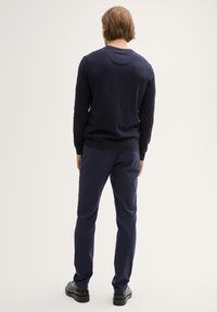 Pull en maille bleu marine avec un col rond, associé à un pantalon marine et des chaussures noires. Texture lisse, silhouette ajustée, design minimal.