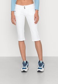 Bílé capri kalhoty až ke kolenům s dvěma knoflíky a kapsami, spárované s modro-bílými sportovními botami s síťovinou a tkaničkami.