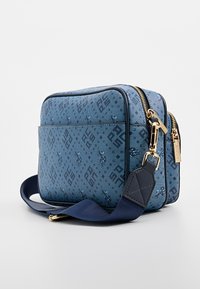 Niebieska torebka na ramię z wzorem, o usztywnionej konstrukcji, z złotymi okuciami, podwójnymi zamkami błyskawicznymi oraz ciemnoniebieskim, regulowanym paskiem.