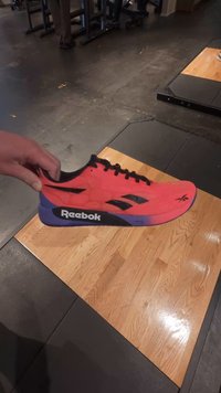 Röd Reebok sportskor med ovandel i mesh, svarta accenter och en blå-lila sula. Designad för prestanda, lätt vikt och andningsförmåga.