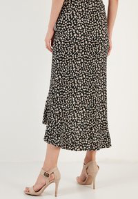 Schwarzer, blumiger Midi-Rock mit einem gerüschten Saum, der kleine weiße und rosa Blumen aufweist. Getragen mit beigen, hochhackigen Sandalen.