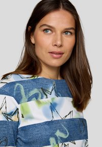 Blau-weiß gestreiftes Oberteil mit einem denimähnlichen Muster, verziert mit grünen und schwarzen abstrakten Designs. Hat einen Bootsausschnitt und eine lässige Passform.