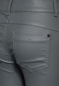 Grå konstläderbyxor med en slät textur, med en bakficka och kontrasterande sömmar. Designen inkluderar en liten märkesetikett nära fickan.