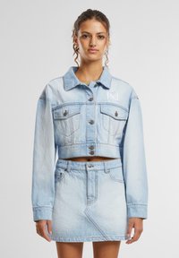 Gaiši zils denimis apgriezts jogos jaka ar pogu aizdari, krūšu kabatām un izšūtu logo; savienota ar atbilstošu denim mini svārku.