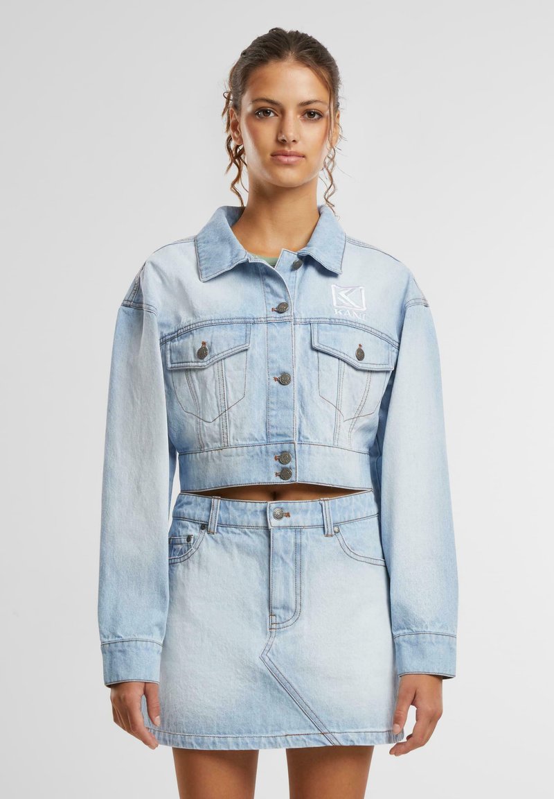 Svetlo modra kavbojka na kratko z gumbom, žepoma na prsih in vezenim logotipom; v kompletu z usklajenim mini krilom iz džinsa.