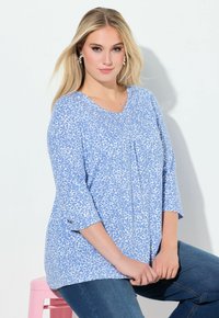 Lichtblauw topje met een wit dierenpatroon, voorzien van een V-hals en driekwartmouwen, gecombineerd met donkerblauwe spijkerbroeken.