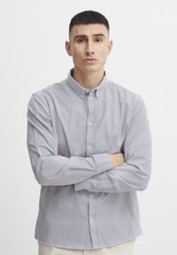 Chemise boutonnée rayée en coton bleu clair et blanc, dotée d'un col et de manches longues, avec une coupe classique et des textures subtiles.