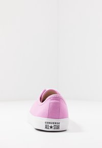 Baskets en toile rose à coupe basse, semelle en caoutchouc blanche, avec le logo "Converse All Star" sur le talon. Texture lisse.