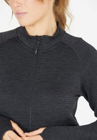 Zwarte zip-up jas van textuurstof, hoge kraag en duimgaten in de mouwen. Bevat een subtiele logo op de borst.