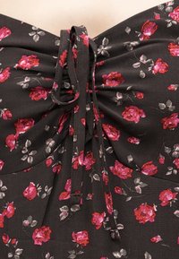 Μαύρο ύφασμα με μικρά ροζ και κόκκινα τριαντάφυλλα, μαζεμένο στο κέντρο με δύο λεπτές κορδέλες που σχηματίζουν φιόγκο στην κορυφή.