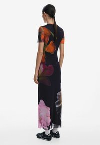 Robe maxi en tissu extensible, ornée d'un imprimé floral aux couleurs vives sur fond sombre. Manches courtes et silhouette ajustée.