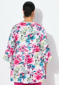 Blumen-Tunika mit lebhaften rosa, blauen und grünen Mustern. Hergestellt aus leichtem Stoff, mit Glockenärmel und gerafftem Taillenbereich.