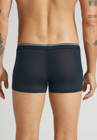 Męskie kąpielówki w kolorze granatowym o jednolitym, gładkim wzorze, z elastycznym pasem i kontrastowym obszyciem, sięgające do połowy uda.