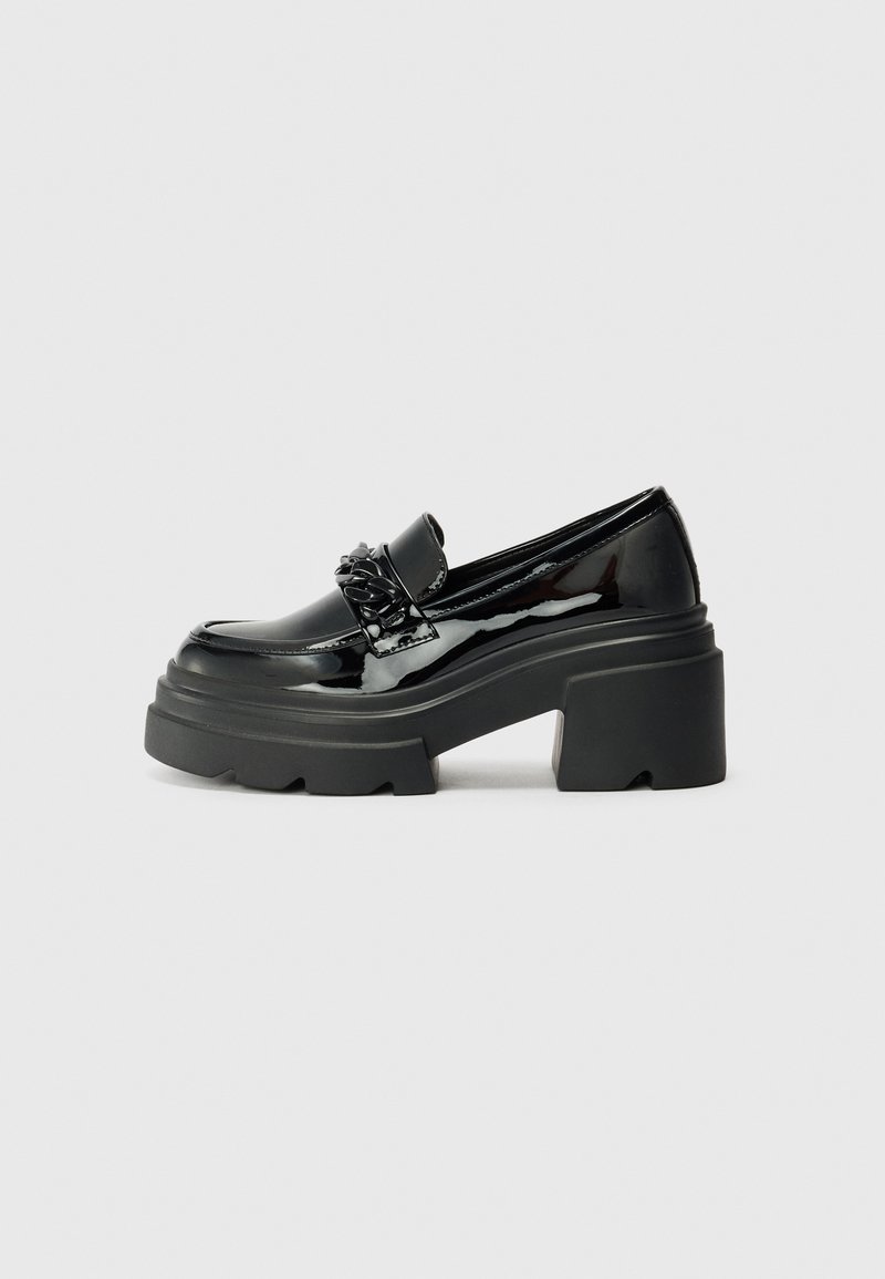 Mocassins noirs en cuir verni avec une semelle plateforme noire épaisse, dotés d'une chaîne décorative à l'avant. Texture lisse, nez arrondi.
