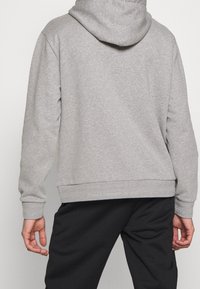 Sudadera gris con capucha, que presenta una textura suave, mangas largas y un dobladillo acanalado. Combinada con pantalones negros, mostrando un ajuste relajado.