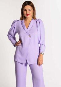 Traje de lavanda con un blazer ajustado de mangas abullonadas, cierre de un solo botón y pantalones de pierna ancha a juego. Textura de tela suave.