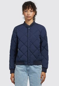 Chaqueta bomber acolchada en color navy con cuello redondo, cierre de botones a presión y puños de canalé. Tejido texturizado con un patrón de diamantes.