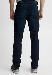 Tumed sinised denim püksid, millel on kitsas lõige, kahte tagataskut ja vöökoht. Ühendatud hallide spordijalatsitega kontrasti loomiseks.