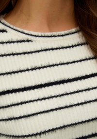 Maglione lavorato a maglia con scollo rotondo, caratterizzato da una texture a coste, base crema e strisce orizzontali nere, creando un modello a contrasto.