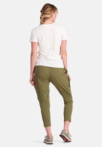 Olijfgroene, lichte broek met een taperende snit en meerdere zakken, gecombineerd met een eenvoudig wit T-shirt en grijze schoenen.